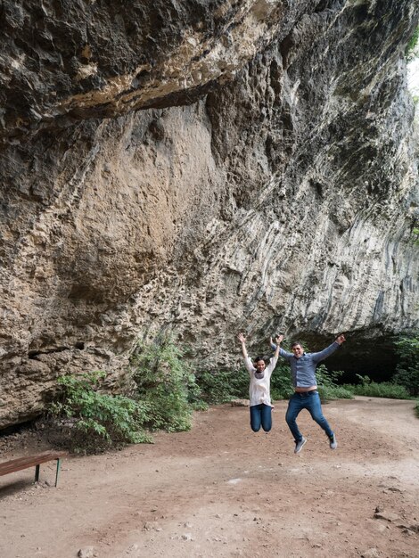 Bella giovane coppia che salta nell'aria di felicità davanti a una grotta. Coppia in natura.