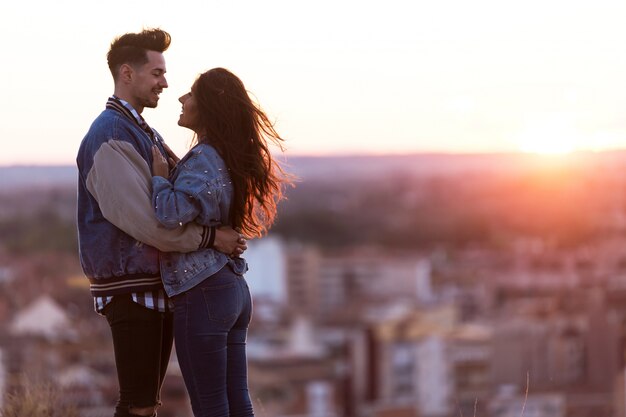 Bella giovane coppia in amore in piedi in un edificio sul tetto al tramonto.