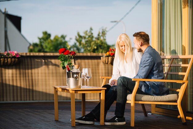 Bella giovane coppia seduta sul tetto con vino secchiello per il ghiaccio e bicchieri