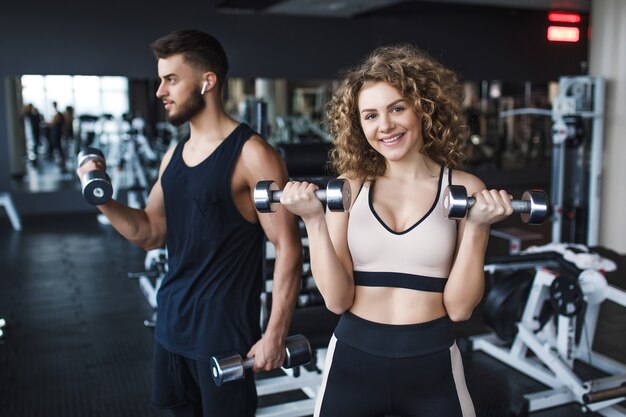 Bella giovane coppia sportiva allenatrice e donna che mostra muscoli e allenamento in palestra durante l'allenamento