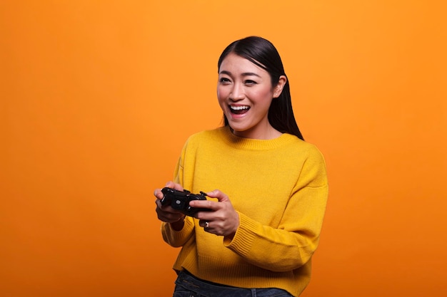 Bella giovane donna adulta eccitata allegra che gioca ai videogiochi con un controller moderno mentre si gode il tempo libero. Persona positiva giocosa con gamepad da gioco che indossa un maglione giallo.