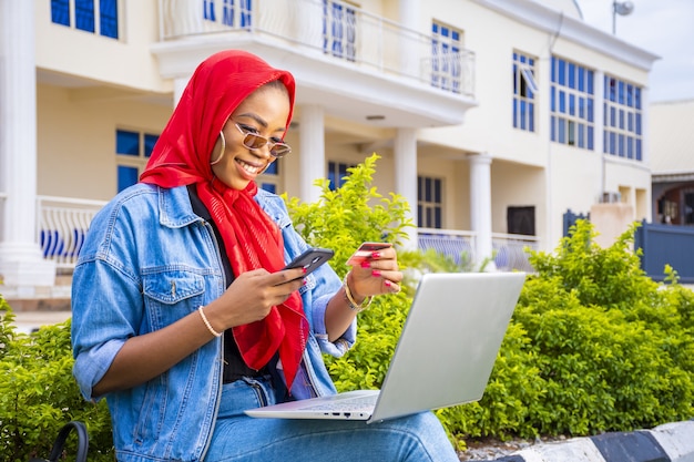 Bella giovane donna africana che sorride mentre usa il suo computer portatile all'esterno