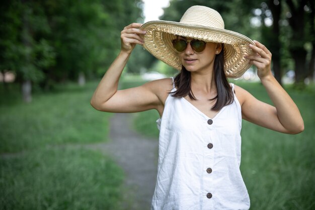 Bella giovane donna alla moda che indossa cappello di paglia e occhiali da sole all'aperto.