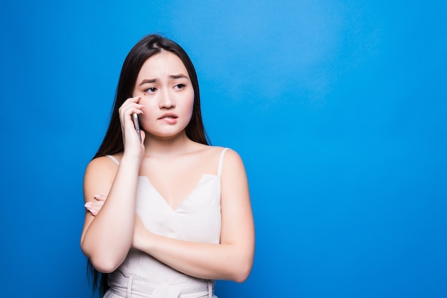 Bella giovane donna asiatica che parla al telefono sulla parete blu