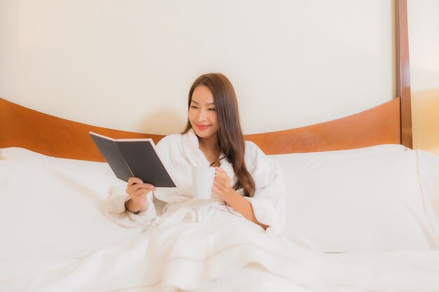 Bella giovane donna asiatica del ritratto che legge libro sul letto nell'interno della camera da letto