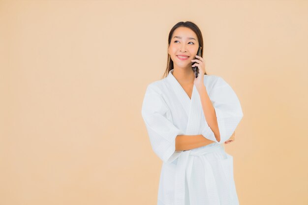 Bella giovane donna asiatica del ritratto che per mezzo del telefono cellulare astuto sul beige