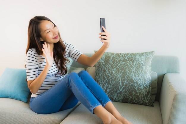 Bella giovane donna asiatica del ritratto che per mezzo o parlando del telefono cellulare