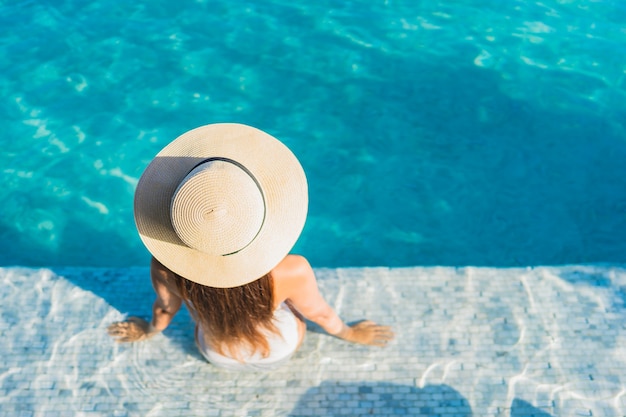 Bella giovane donna asiatica del ritratto che si rilassa intorno alla piscina all'aperto con la vista della città