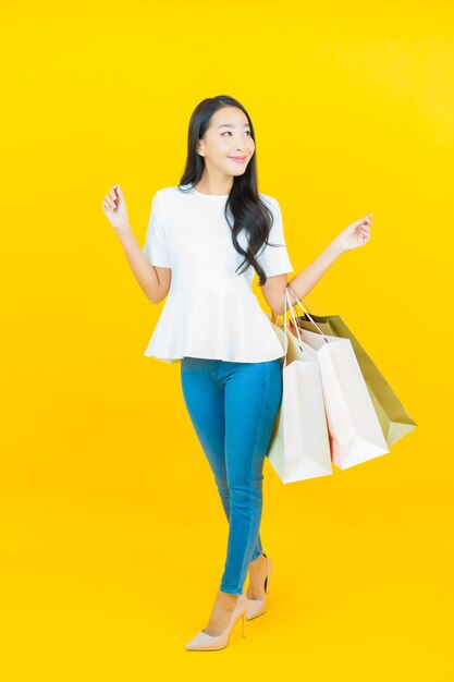 Bella giovane donna asiatica del ritratto che sorride con la borsa della spesa su yellow