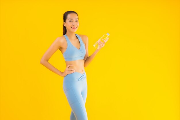 Bella giovane donna asiatica del ritratto con acqua di bottiglia su giallo