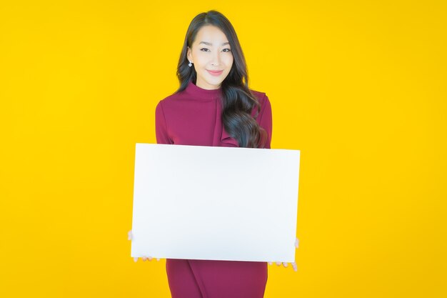 Bella giovane donna asiatica del ritratto con il tabellone per le affissioni bianco vuoto su yellow