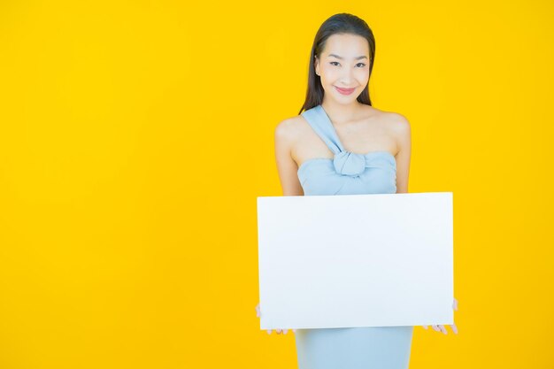 Bella giovane donna asiatica del ritratto con il tabellone per le affissioni bianco vuoto su yellow