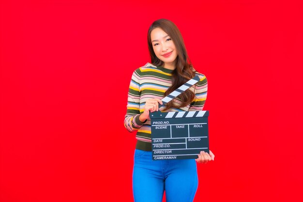 Bella giovane donna asiatica del ritratto con il taglio dell'ardesia di film sulla parete isolata rossa