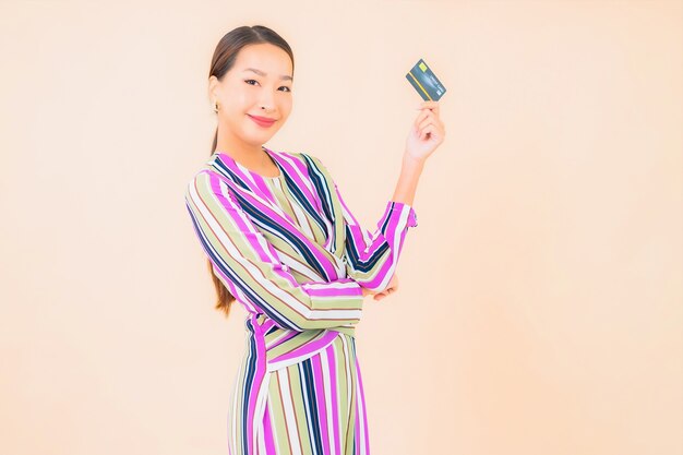 Bella giovane donna asiatica del ritratto con il telefono cellulare astuto e la carta di credito sul colore