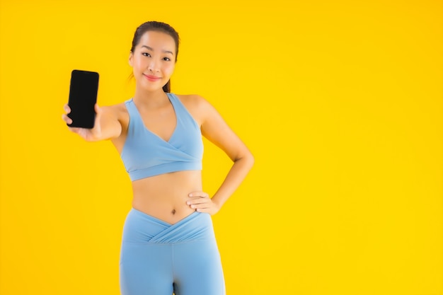 Bella giovane donna asiatica del ritratto con il telefono cellulare astuto su giallo isolato