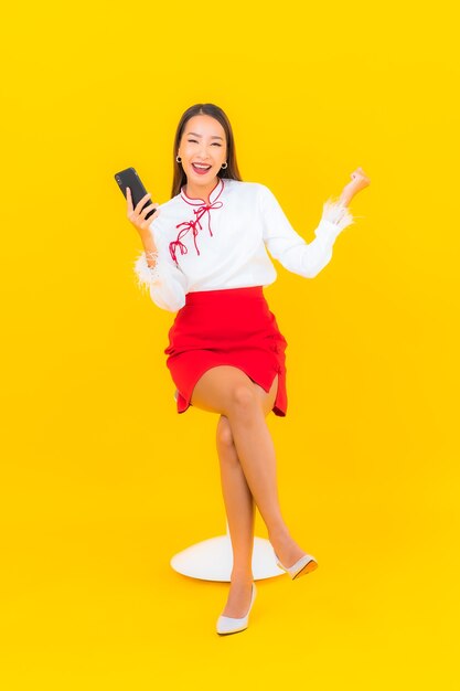 Bella giovane donna asiatica del ritratto con il telefono cellulare astuto su yellow