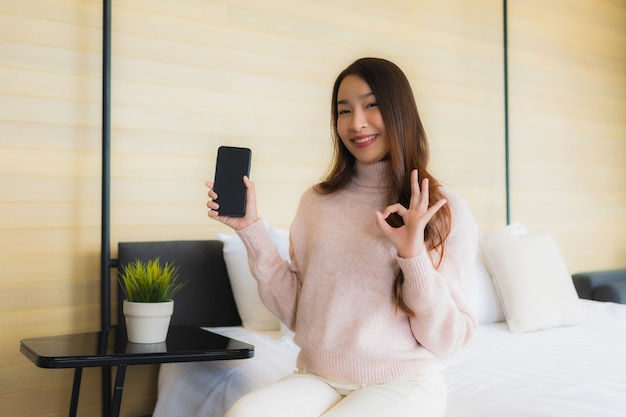 Bella giovane donna asiatica del ritratto con il telefono cellulare sul letto