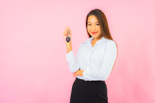 Bella giovane donna asiatica del ritratto con la chiave dell'automobile sulla parete isolata rosa