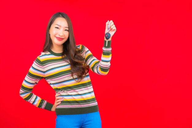 Bella giovane donna asiatica del ritratto con la chiave dell'automobile sulla parete isolata rossa