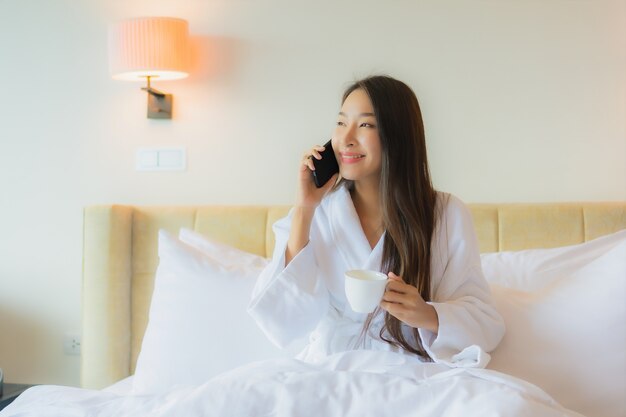 Bella giovane donna asiatica del ritratto con la tazza di caffè sul letto