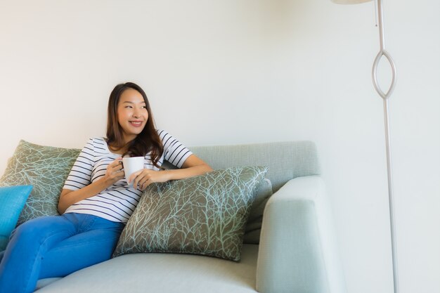 Bella giovane donna asiatica del ritratto sul sofà con la tazza di caffè