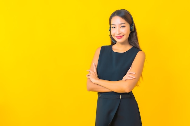 Bella giovane donna asiatica di affari del ritratto con l'assistenza clienti della call center dell'auricolare su fondo giallo