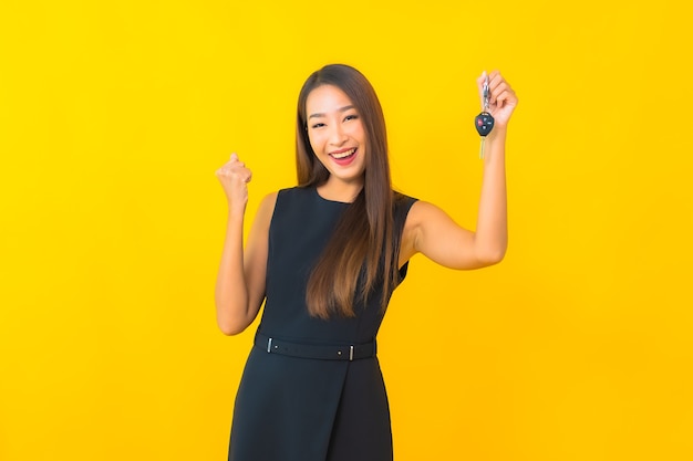 Bella giovane donna asiatica di affari del ritratto con la chiave dell'automobile su fondo giallo