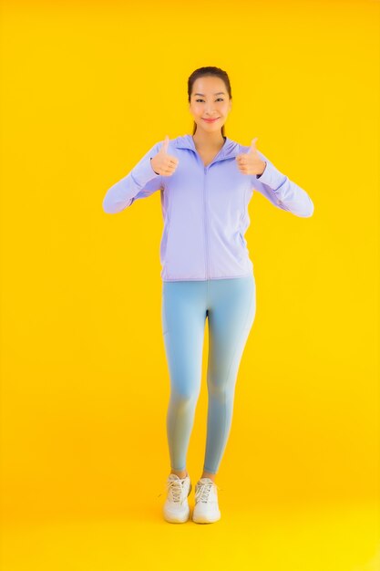 Bella giovane donna asiatica di sport del ritratto pronta per l'esercizio su giallo