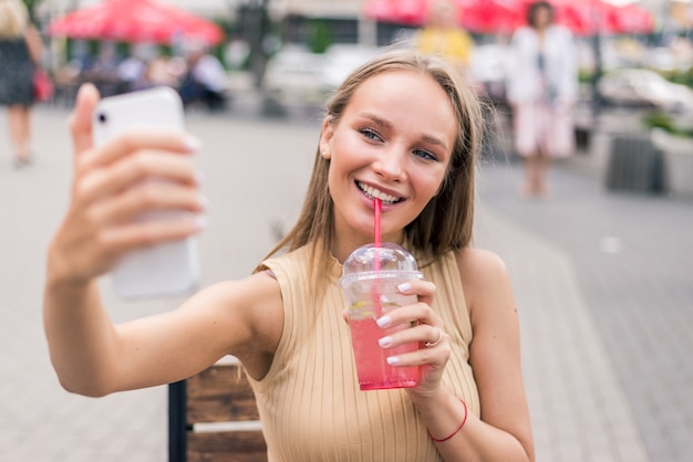 Bella giovane donna beve mojito facendo selfie nel caffè di strada estivo