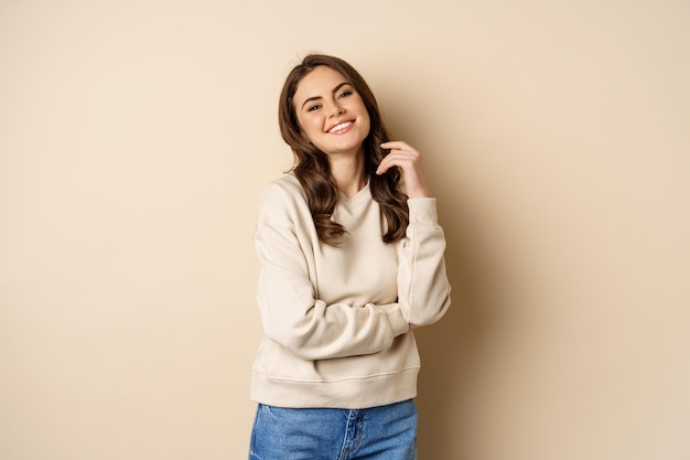 Bella giovane donna bruna in posa felice su sfondo beige sorridente alla telecamera indossando maglione