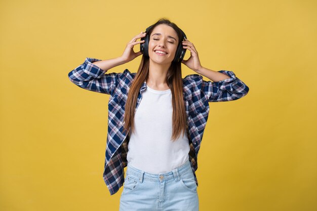 Bella giovane donna calma che ascolta la musica in cuffia con gli occhi chiusi su sfondo giallo. Avvicinamento