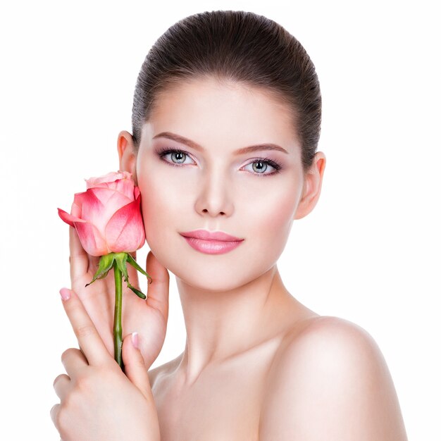 Bella giovane donna castana con pelle sana e fiori rosa vicino al viso - isolato su bianco.