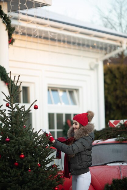 Bella giovane donna casual invernale in posa all'aperto circondata da fiocchi di neve a tiro medio lungo. Bella ragazza felice che si gode l'umore di Natale sullo sfondo dell'albero di Natale con emozioni positive