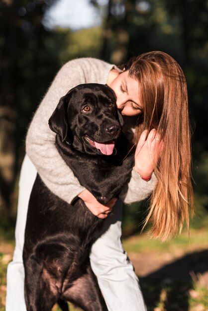 Bella giovane donna che bacia il suo labrador nero nel parco