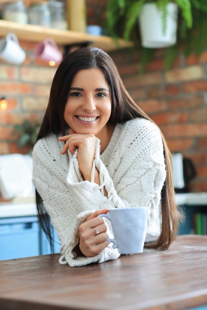 Bella giovane donna che beve caffè o tè in cucina