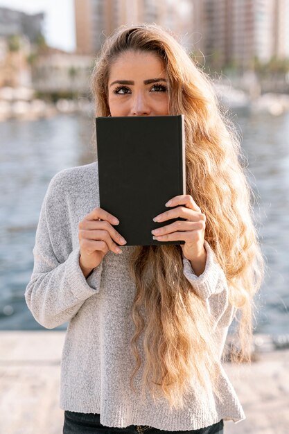 Bella giovane donna che copre la bocca di un libro
