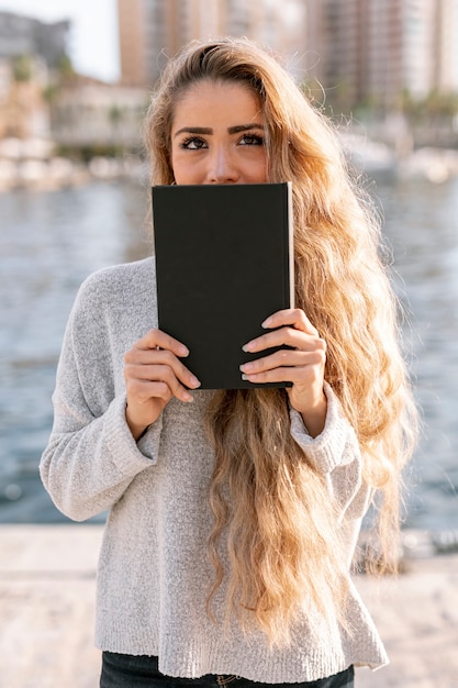 Bella giovane donna che copre la bocca di un libro