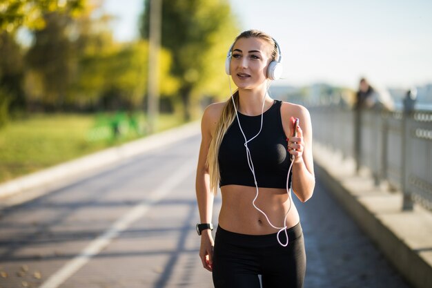 Bella giovane donna che corre nel parco verde nella soleggiata giornata estiva