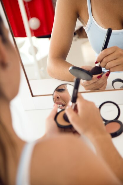 Bella giovane donna che fa trucco vicino allo specchio a casa.