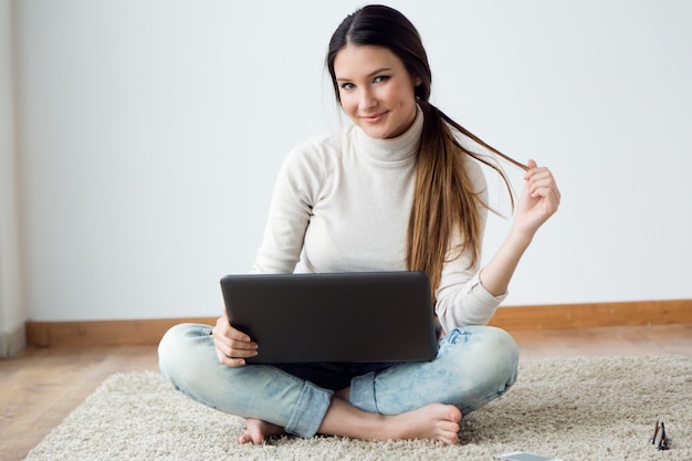 Bella giovane donna che lavora sul suo computer portatile a casa.