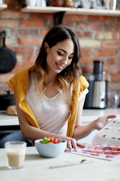 Bella giovane donna che mangia un'insalata sana e che legge una rivista