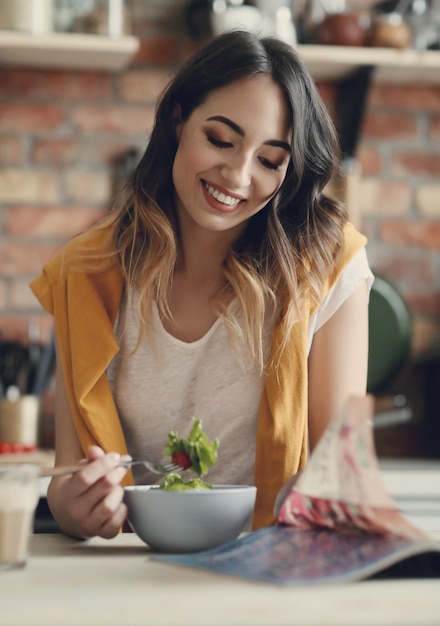 Bella giovane donna che mangia un'insalata sana e che legge una rivista