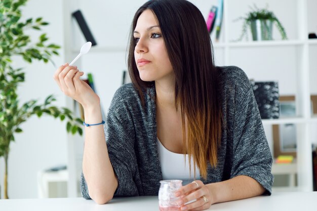 Bella giovane donna che mangia yogurt a casa.