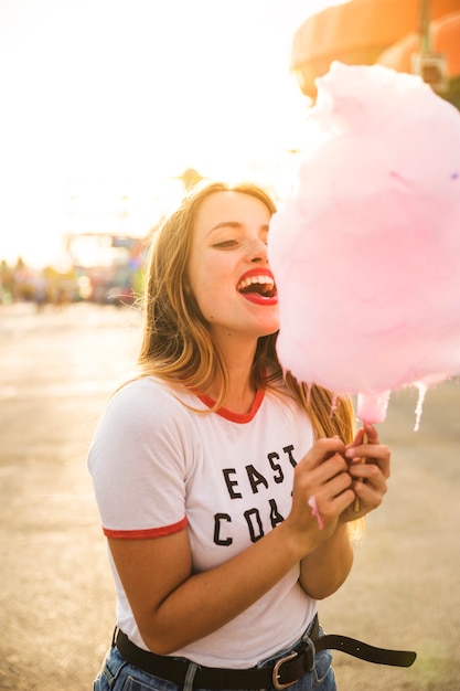 Bella giovane donna che mangia zucchero filato rosa