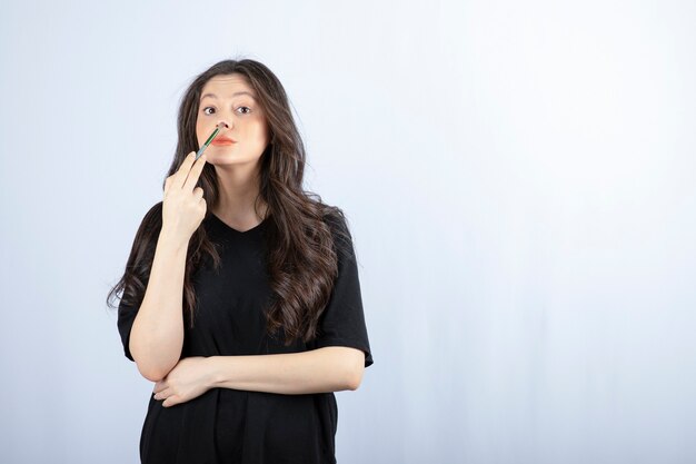 Bella giovane donna che mette evidenziatore con pennello cosmetico al naso.