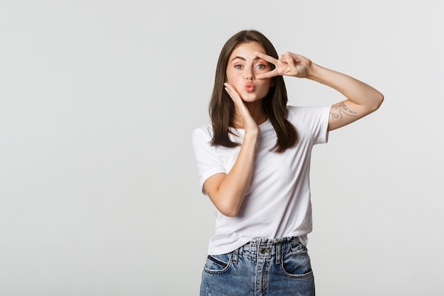 Bella giovane donna che mostra gesto di pace e imbronciato sciocco, bianco.