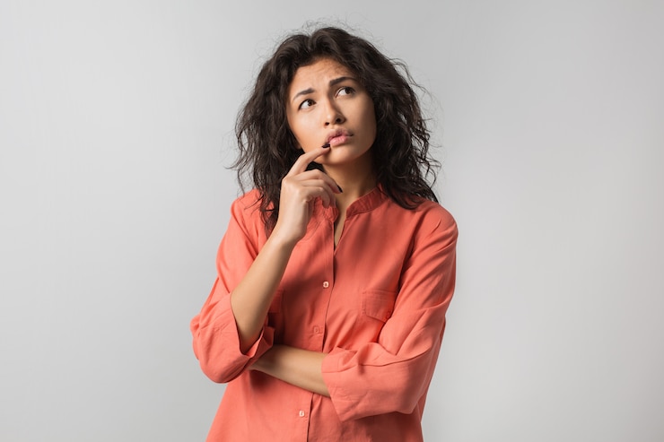 Foto gratuito bella giovane donna che pensa al problema, emozione confusa, isolato, indossa una maglietta arancione, stile hipster, capelli ricci, tenendo il dito sulle labbra, guardando in alto, avendo un'idea
