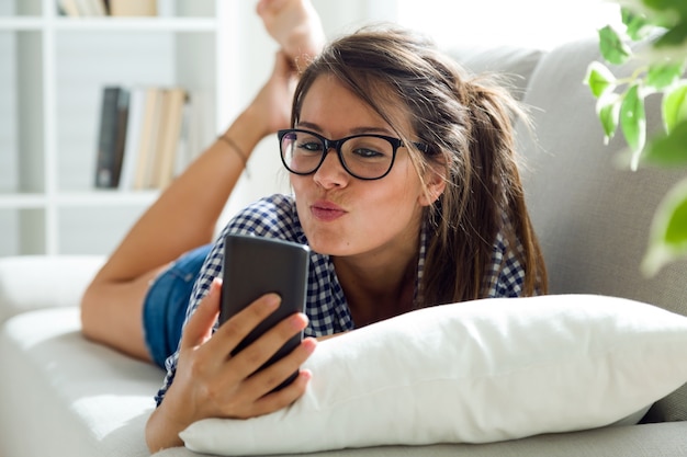 Bella giovane donna che per mezzo del suo telefono cellulare a casa