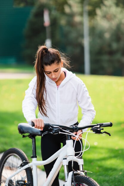 Bella giovane donna che posa alla bicicletta bianca