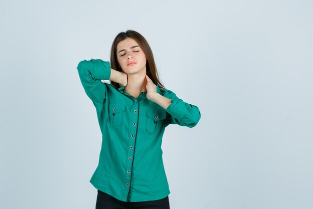 Bella giovane donna che sente dolore al collo in camicia verde e sembra a disagio, vista frontale.